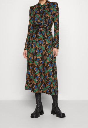 Długa sukienka damska z długim rękawem o długości midi z kolorowym kwiatowym wzorem, zestawiona z czarnymi, sięgającymi połowy łydki, butami na obcasie na szarej podłodze.