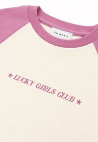 Κρεμ και ροζ raglan μπλούζα με το κείμενο "LUCKY GIRLS CLUB" και ροζ αστέρια μπροστά και ετικέτα "OH APRIL" μέσα στο γιακά.