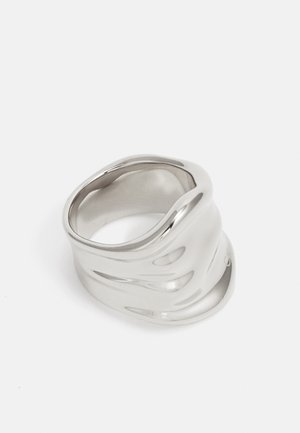 Silberner gewellter Ring aus poliertem Metall mit glatter Oberfläche und einem länglichen, unregelmäßigen Design. Keine sichtbaren Muster oder Akzente.