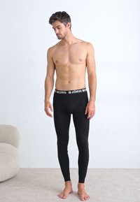 Leggings pretos com um design ajustado, apresentando uma cintura elástica com marca. O material parece suave e elástico, adequado para uso ativo.