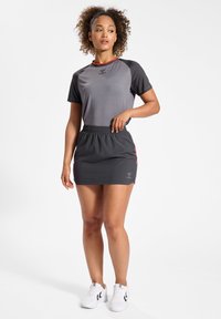 Grijze sporttop met korte zwarte mouwen met patroon, gecombineerd met een grijze rok met een elastische tailleband. Voorzien van een klein logodetail bij de taille.