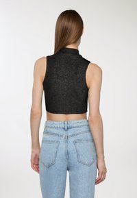Czarny, bezrękawnikowy, krótki top o teksturowanym, połyskującym wykończeniu, w połączeniu z jasnoniebieskimi dżinsami z wysokim stanem, wyposażonymi w tylne kieszenie.