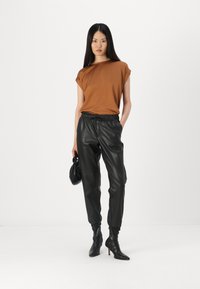 Brown short-sleeve top paired with black faux leather joggers. The outfit is complemented by pointed black ankle boots and a black bag.