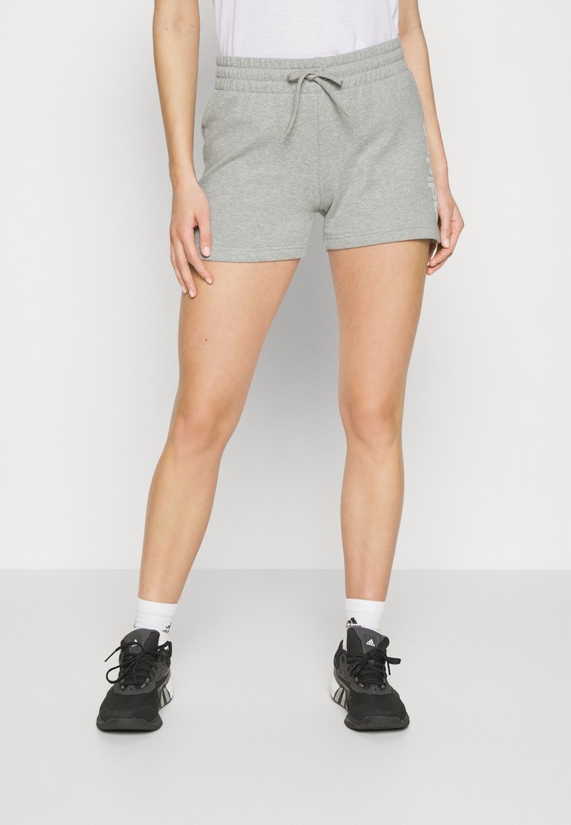 Pantalones cortos de mezcla de algodón grises con cinturilla elástica y cordón, con un estampado lateral. Combinados con zapatos deportivos negros y calcetines blancos.