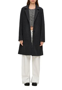 Langer, dunkelgrauer Mantel aus Wollmischung, mit kontrastierendem Reverskragen, doppelter Knopfleiste und gerade geschnittenen Ärmeln. Kombiniert mit einem gestreiften Oberteil und hellen Hosen.