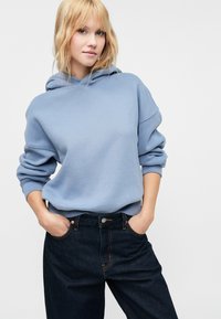 Felpa azzurra chiara con una grande tasca frontale, scollatura rotonda e polsini a coste, abbinata a jeans scuri in denim con cuciture a contrasto.