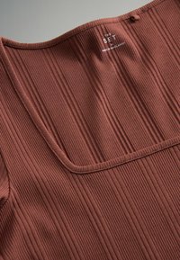 Rybkovaný hnedý top s širokým výstrihom, textúrovaným materiálom a etiketou s názvom "THE SET." Zdôrazňuje hladké, vertikálne línie.