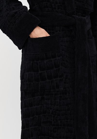 Μαύρη ρόμπα φτιαγμένη από υφασμάτινη υφή με μοτίβο κροκοδείλου· διαθέτει φαρδιές μανσέτες, ζωνάκι και δύο μπροστινές τσέπες.
