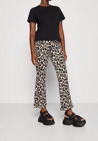 T-shirt en coton noir associé à un pantalon évasé imprimé léopard beige et des sandales noires épaisses. La tenue présente un design décontracté et des motifs distincts.