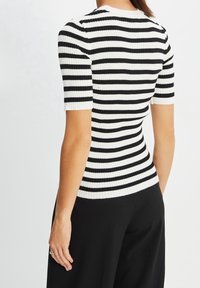 Schwarz-weiß gestreiftes, geripptes Oberteil mit kurzen Ärmeln, das eine figurbetonte Passform und einen runden Ausschnitt aufweist. Sichtbare Textur und Muster.