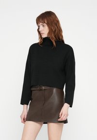 Svart kort turtleneck-genser med lange ermer, kombinert med et brunt skinn miniskjørt med belte i midjen og glatt tekstur.