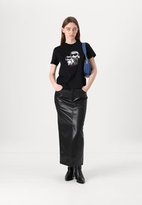 Svart bomulls t-shirt med grafisk tryck som föreställer två tecknade figurer, i kombination med en svart läder pennkjol och ankelstövlar. Blå handväska.