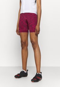 Růžovo-černé cyklistické kraťasy se vzorem a těsným střihem, vybavené polstrovanou vložkou a hladkým, elastickým materiálem. Nesené s černými sportovními botami.