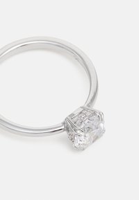 Bague en argent avec une grande pierre claire à l'avant, entourée de petites pierres claires. Bande lisse et finition poli.