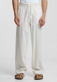 Witte linnen broek met een elastische tailleband, straight-leg pasvorm en een zachte textuur, gecombineerd met bruine sandalen.