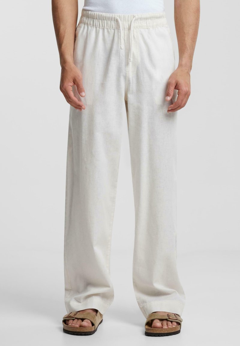 Witte linnen broek met een elastische tailleband, straight-leg pasvorm en een zachte textuur, gecombineerd met bruine sandalen.