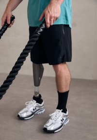 Pantalones cortos deportivos negros combinados con una camiseta turquesa. La persona lleva zapatillas blancas y plateadas, y tiene una pierna prostética metálica.