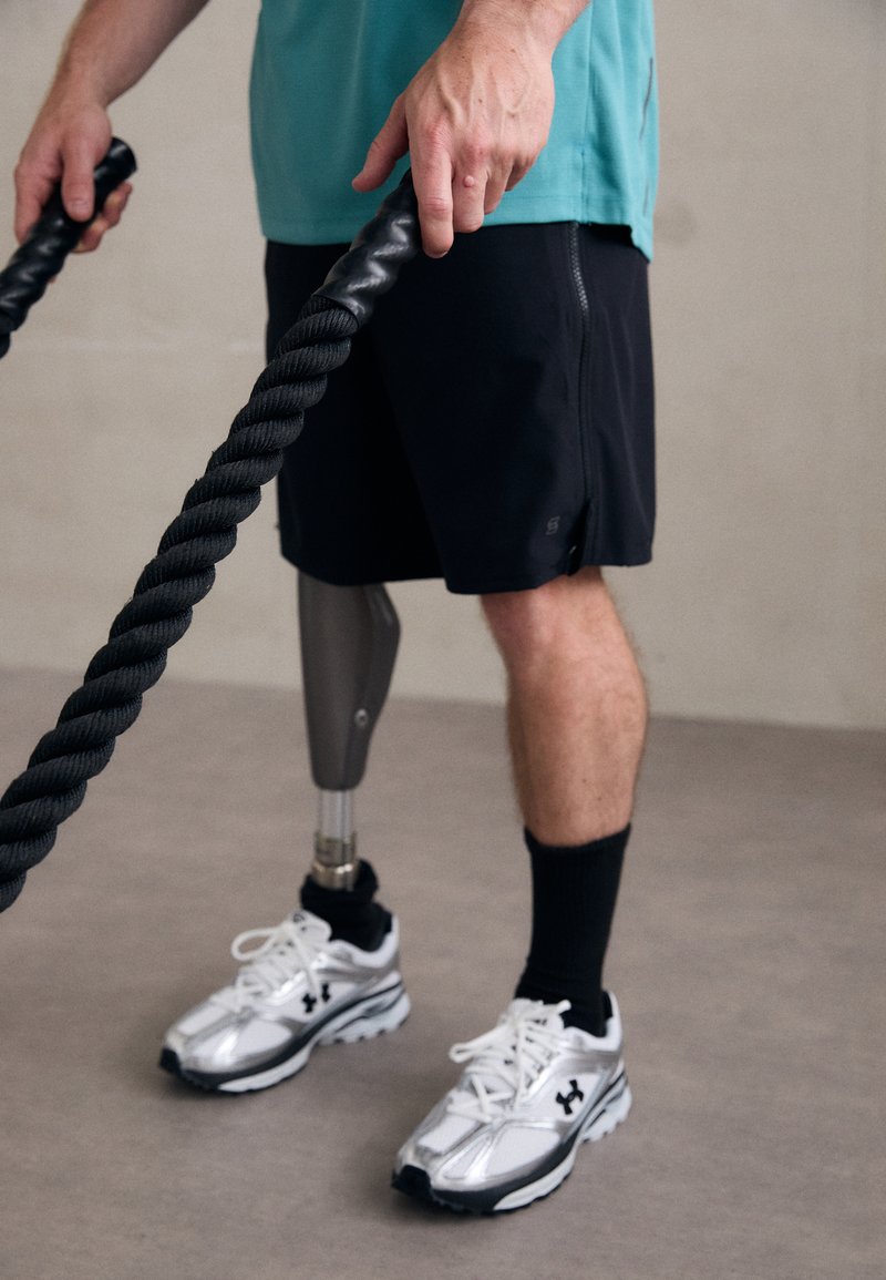 Pantalones cortos deportivos negros combinados con una camiseta turquesa. La persona lleva zapatillas blancas y plateadas, y tiene una pierna prostética metálica.