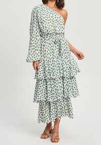 Vestido floral verde y blanco de un solo hombro con volantes en capas y cintura ceñida; hecho de una tela ligera apta para climas cálidos.