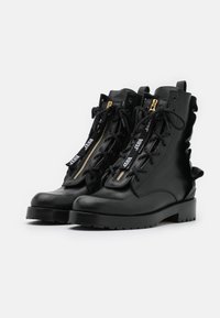 Bottes en cuir noir avec un bout arrondi, une tige haute, un laçage frontal, une fermeture éclair latérale et des détails à volants. Semelle épaisse et texturée.