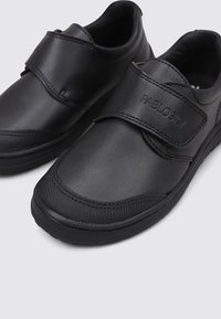 Zapatos negros con upper texturizado y cierre de velcro. Hechos de material sintético liso con punta redondeada y suela de goma.