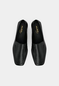 Chaussures noires en cuir à enfiler avec un bout carré, présentant des détails de couture minimalistes et la marque "ALDO" embossée sur la semelle intérieure.