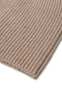 Tessuto di lana a coste in un morbido colore beige, caratterizzato da una superficie testurizzata e un bordo piegato, che mette in evidenza fibre sottili e un aspetto accogliente.