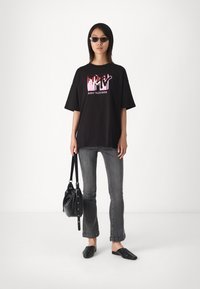 Mustat ylisuuret t-paidat, joissa on värikäs MTV-logo, harmaat slim-fit farkut, musta laukku ja mustat liukuvetokengät. Silkkinen kangas, rento muotoilu.