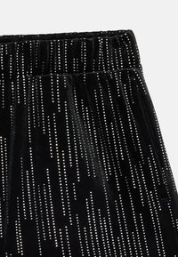 Pantaloni din catifea neagră cu un design texturat, având strasuri argintii dispuse pe linii verticale. Talie elastică pentru confort.