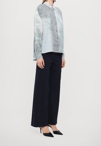 Camicia a maniche lunghe con stampa tie-dye blu chiaro e grigio, abbinata a pantaloni navy a gamba larga e décolleté neri a punta.
