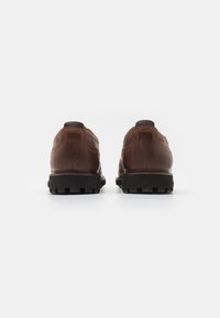 Chaussures en cuir marron avec une finition texturée, arrière arrondi, semelle en caoutchouc noir robuste et détails de couture marquants.