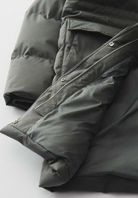 Doudoune en tissu vert foncé, avec une texture lisse, fermeture éclair et poche à bouton-pression. Conçue pour la chaleur et le confort.