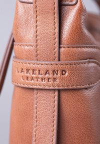 Brown leather handbag featuring a textured surface, stitched accents, and embossed branding. Design focuses on simplicity and durability.