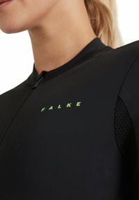 Haut zippé de sport noir avec des accents en maille et un logo "FALKE" vert sur la poitrine. Fabriqué en tissu lisse et extensible pour un confort optimal.