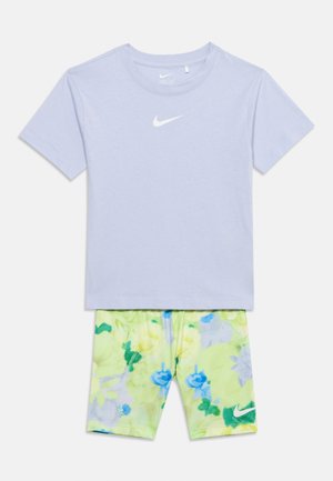 T-shirt Nike à manches courtes violet clair associée à un short Nike à motif floral jaune et vert avec des accents bleus.