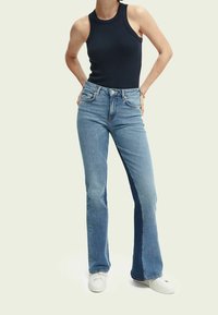 Blå högmidjade utsvängda jeans med ljus tvätt, med subtila blekningar och en mjuk, stretchig textur. Stylar med en åtsittande svart tank top.