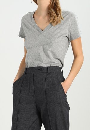 Graues T-Shirt mit V-Ausschnitt aus weichem Stoff, kombiniert mit hoch taillierten, dunkel karierten Hosen, ausgestattet mit seitlichen Taschen und einem Knopfverschluss.