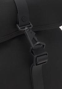 Borsa impermeabile nera con finitura liscia, dotata di fibbia e tracolla in plastica, bordi cuciti e design minimale.