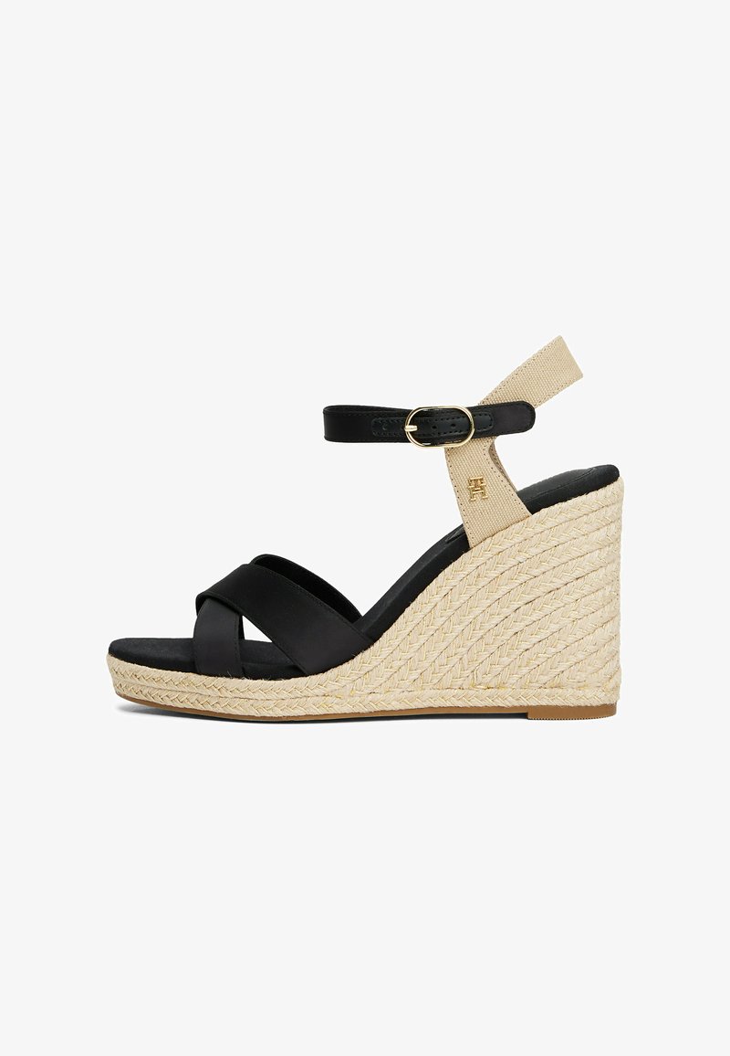 Sandali con zeppa in pelle nera, con cinturini incrociati, cinturino beige alla caviglia e tacco in iuta intrecciata. Il dettaglio della fibbia dorata aggiunge un accento sottile.