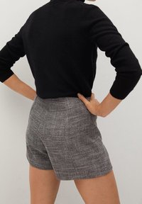 Shorts à taille haute en tissu à carreaux noir et blanc, présentant une coupe ajustée et une texture lisse, associés à un haut noir ajusté.
