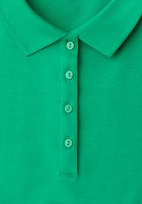 Polo vert avec un col côtelé et quatre boutons verts assortis sur la patte de boutonnage, présenté à plat et centré.