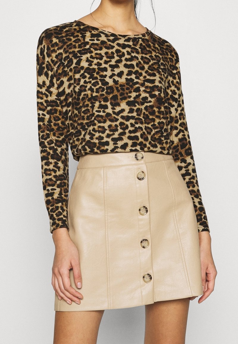 Femme portant un haut à manches longues imprimé léopard et une mini-jupe en cuir beige avec boutons sur le devant.