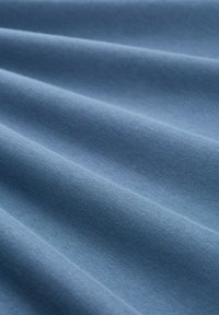 Helleblaue Stoff mit einer glatten Textur, der weiche Falten und eine gleichmäßige Oberfläche aufweist. Das Material scheint Baumwolle oder einer ähnlichen Mischung zu sein.