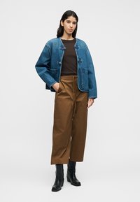 Τζιν μπουφάν με άνετη εφαρμογή, ανοιχτό μπλε χρώμα και τσέπες στο μπροστινό μέρος. Καφέ παντελόνι με φαρδύ πόδι και κορδόνι στη μέση. Μαύρα μποτάκια μέχρι τον αστράγαλο.