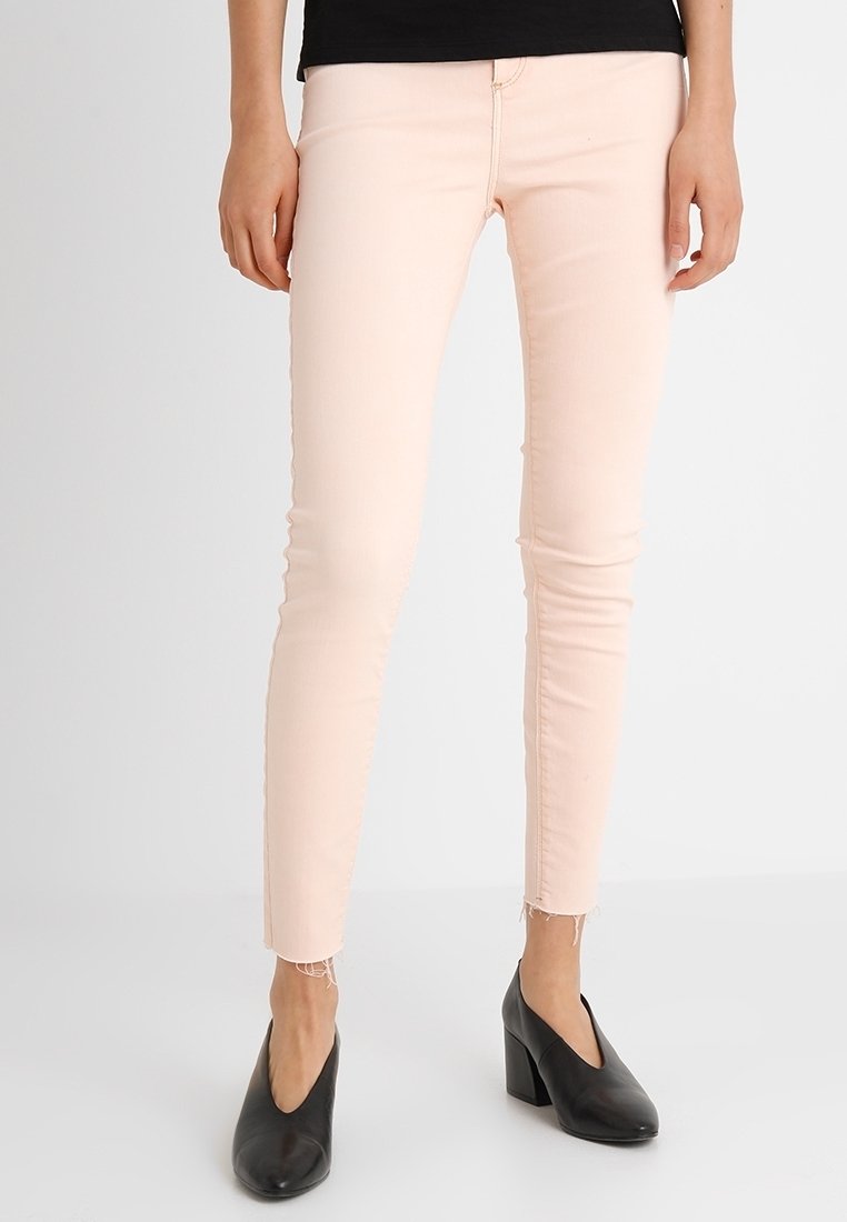 Jeans skinny de color rosa claro, hechos de una mezcla de algodón, con un dobladillo deshilachado y un diseño clásico de cinco bolsillos, combinados con zapatos de tacón negros.