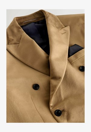 Šviesiai rudos spalvos dvigubo krūtinkaulio švarkas, pagamintas iš lygios medžiagos, su juodais mygtukais ir kontrastinga tamsiai mėlyna kišenine nosinaita. Išskirtiniai švelnūs tekstūravimai ir apykaklės.