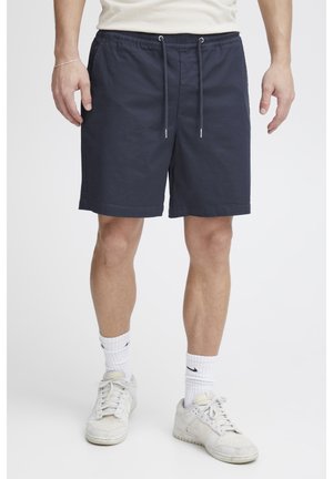 Marineblå shorts med elastisk midjebånd og snor, med to sidelommer og en avslappet passform. Brukes med hvite sokker og joggesko.