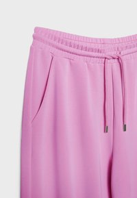 Pinke Jogginghose mit elastischem Bund, Kordelzug und Seitentaschen vor weißem Hintergrund.