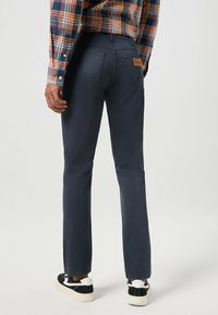 Granatowe spodnie o prostym kroju, wykonane z bawełny. Posiadają dwie tylne kieszenie, widoczne stębnowanie oraz skórzaną naszywkę z logo na pasie.