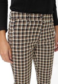 Bruine en zwarte houndstooth-patroon broek met een tailleband, knoopsluiting en handzakken; de stof lijkt textuur en structuur te hebben.